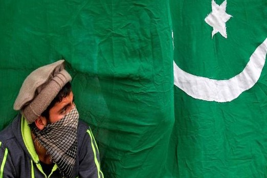 A masked protester sits next to a flag of Pakistan during an anti-Indian protest in Srinagar